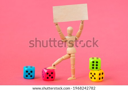 Wooden man with a blank banner and colored dices on the pink background