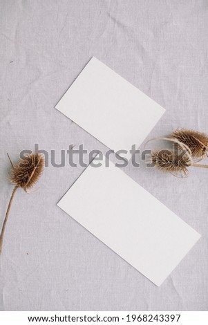 White blank paper cards and decorative dry twigs of thistle on linen background. Wedding invitation, business card,  newsletter concept, mock up.