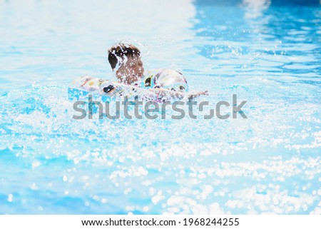 Happy boy in swimming pool. Boy is alone, swimming inflatable ring and surronded by water splashes. Wet teenager is enjoying summer weekend in amusement water park. Banner with copy space