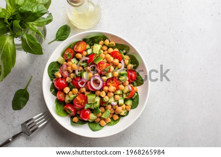 Fresh summer mediterranean salad with chickpea, tomatoes, cucumbers, spinach, red onion, parsley. Light background, copy space. Royalty-Free Stock Photo #1968265984