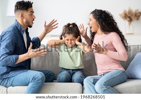 Parental Quarrels. Arab Man And Woman Arguing In Front Of Their Child, Upset Little Girl Covering Ears With Hands Not To Listen Conflict, Stressed Female Kid Sitting Between Shouting Parents Royalty-Free Stock Photo #1968268501