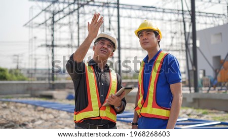 senior contractor manager talking to young asian builder with digital tablet at construction site outdoors . group of diversity construction worker in hard hat meeting outside 