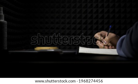 Concept of songwriting, side view of a man writing lyrics in a professional music studio. HDR. Process of creating a song by the author, musician writing text on a sheet of paper. Royalty-Free Stock Photo #1968274456