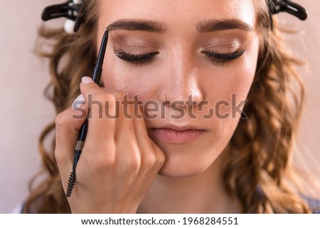 The makeup artist paints the eyebrow of the model using a pencil.