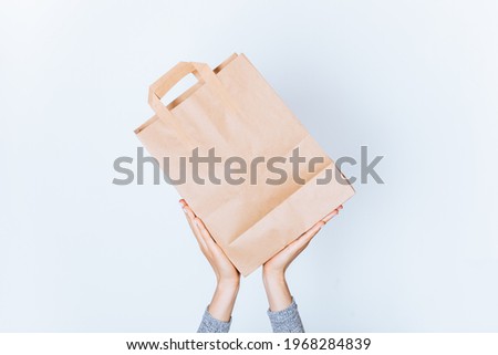 Female hands holding brown kraft paper bag with handles on white background