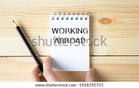 Businessman holding a white notepad with text working abroad , business concept