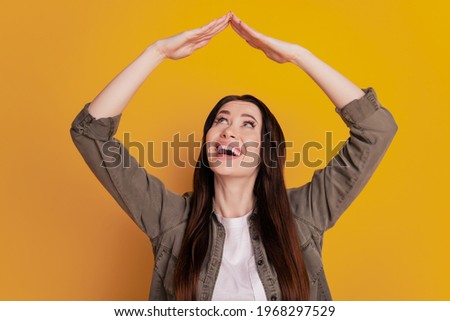 Photo of young surprised girl hold arms roof isolated on yellow background
