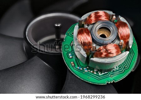 Closeup of inductors on stator and rotor with permanent magnet and black blades in background. Electric EC motor of open computer fan with copper wire on iron sheets on green electronic circuit board. Royalty-Free Stock Photo #1968299236