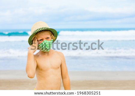 Child in straw hat, stylish masks have fun on sea beach. New rules to wear face covering at public places. Cancelled cruise, tour due coronavirus COVID 19. Family summer vacation, travel lifestyle.