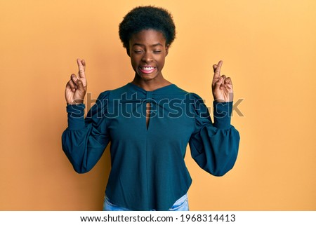 Young african american girl wearing casual clothes gesturing finger crossed smiling with hope and eyes closed. luck and superstitious concept. 