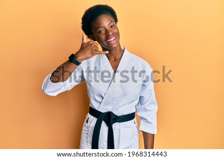 Young african american girl wearing karate kimono and black belt smiling doing phone gesture with hand and fingers like talking on the telephone. communicating concepts. 