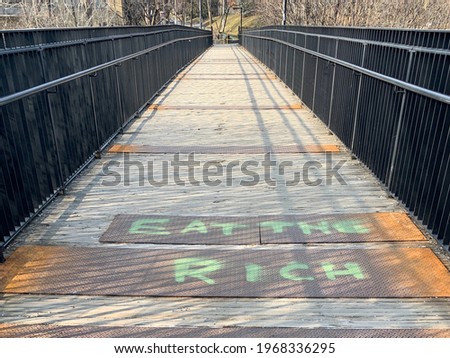 Spray painted words saying 'EAT THE RICH' on metal floor of an empty bridge centered in photo and leading to an end point in the distance, green anarchist anti-capitalist graffiti vandalism