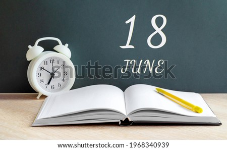 june 18. 18-th day of the month, calendar date.A white alarm clock, an open notebook with blank pages, and a yellow pencil lie on the table. Summer month, day of the year concept.