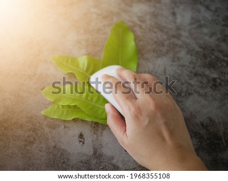 The girl's hand holding computer mouse on the green leaves. 
