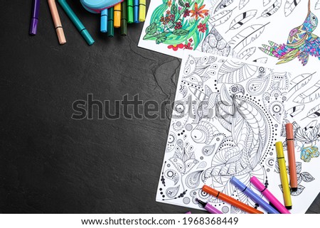 Antistress coloring pages and felt tip pens on black table, flat lay. Space for text