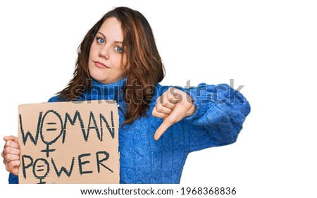 Young plus size woman holding woman power banner with angry face, negative sign showing dislike with thumbs down, rejection concept 