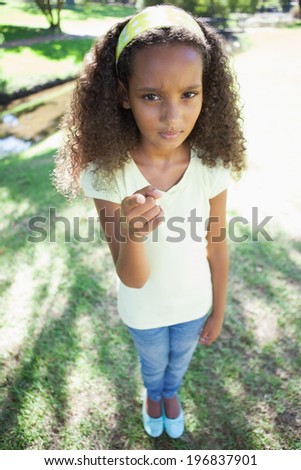 Young girl frowning and pointing at the camera in the park on a sunny day