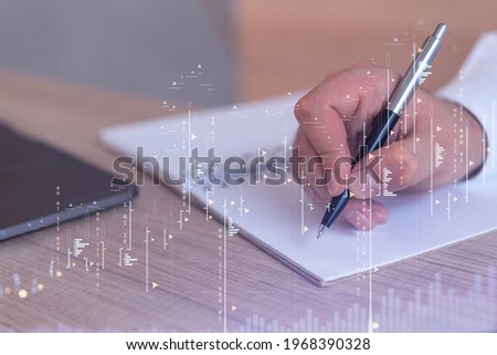 A trader in formal wear writing down some ideas to research stock market to proceed right investment solutions. Wealth management concept. Hologram Forex chart over close up shot.
