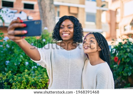 African american mother and daugther hugging and making selfie by the smartphone at the park.