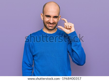 Young hispanic man wearing casual clothes smiling and confident gesturing with hand doing small size sign with fingers looking and the camera. measure concept. 