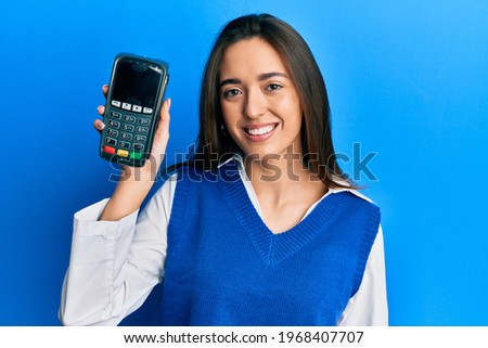 Young hispanic girl holding dataphone looking positive and happy standing and smiling with a confident smile showing teeth 