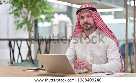 Serious Arab Businessman with Laptop Looking at Camera