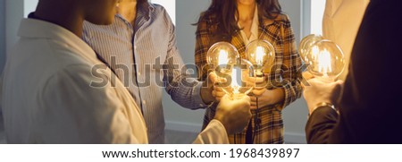 Group of happy young multiracial business people holding electric light bulbs. Team of colleagues join Edison light bulbs as conceptual metaphor for teamwork and sharing ideas in creative community Royalty-Free Stock Photo #1968439897