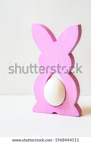 colored figurine - a stand made of wood in the form of a hare inside which an egg on a white background	