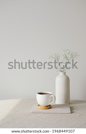 Scandinavian, nordic style home interior decoration. Cup of coffee and vase of flower on linen fabric on table. White wall on background. Morning, breakfast concept