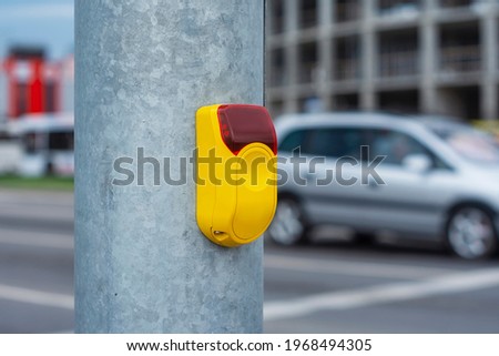 Yellow button at a traffic light for pedestrians on the background of a road with cars