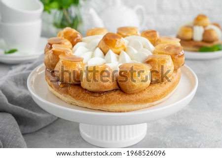 Saint Honore cake with profitrols, caramel, custard and whipped cream on a white plate on a gray concrete background. Traditional French dessert. Copy space Royalty-Free Stock Photo #1968526096