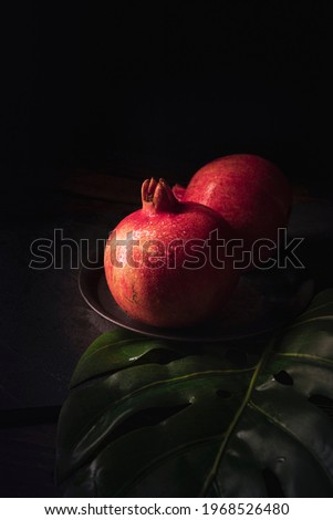 Beautiful fresh red pomegranates on a tropical leaf with a dark background.Appetizing ripe pomegranates and ready to eat. 
Moody fruit photography