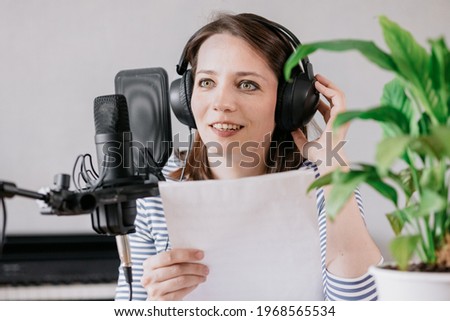 the stylish and educated caucasian woman records podcasts in a recording studio or in her home. the European millennial woman creates audio content or records text, records an audio book or radio show