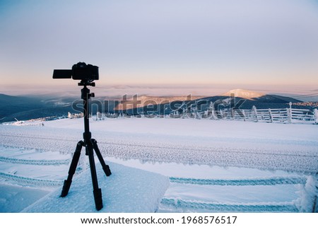 Camera on tripod shooting time lapse in mountain winter landscape, frozen morning outdoor