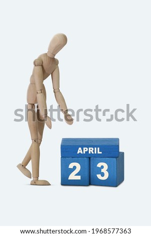 day of the month 23 April calendar A calendar date on blue cubes and a wooden man standing next to it. White background.