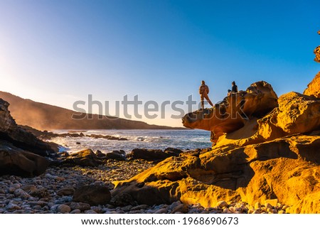 Two girls at sunset in the cove of stones in the Jaizkibel mountain in the town of Pasajes, Gipuzkoa. Basque Country Royalty-Free Stock Photo #1968690673