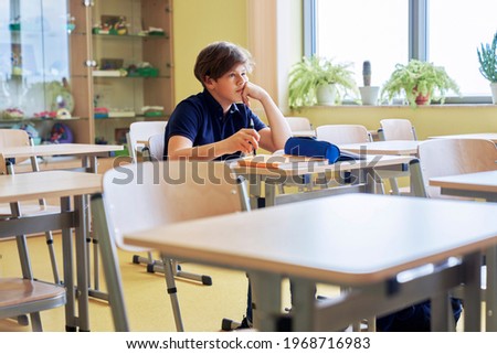 Boy sitting alone in empty classroom Royalty-Free Stock Photo #1968716983
