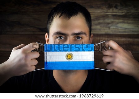 Young man gets dressed, removes a medical mask under the flag of Argentina	
