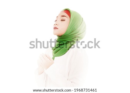 Asian Muslim woman in a veil sitting while raised hands and praying with bright light background