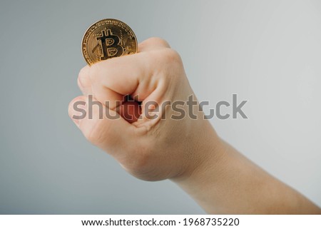 Gold bitcoin in a man's hand holding between the fingers.