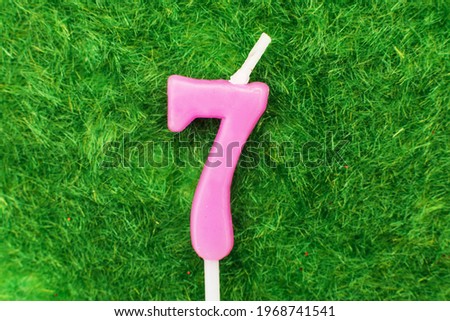 candle in the form of number seven on the green grass background, a place for a greeting text