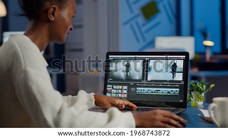 African videographer working at laptop from business office, editing video and audio footage at night. Content creator using professional device modern technology network wireless processing film