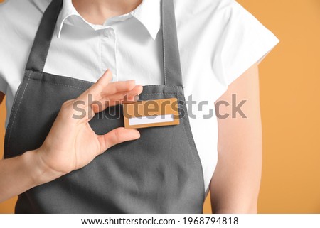 Young female waiter with blank badge on color background
