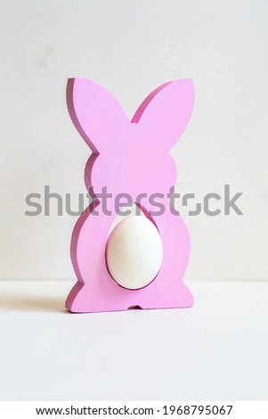 colored figurine - a stand made of wood in the form of a hare inside which an egg on a white background