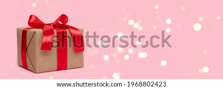 Banner with gift box tied with red ribbon on a pink background. Wrapped present for holidays. 