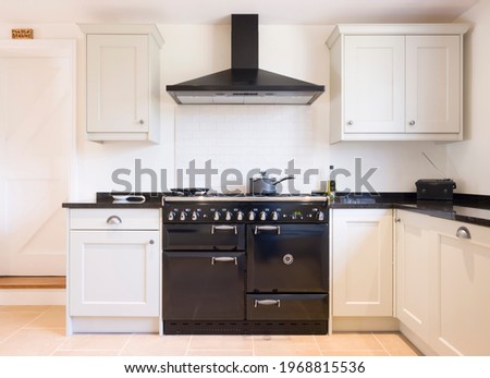 Modern modular kitchen interior in black and off white, with range cooker and chimney extractor hood. UK painted wood farmhouse kitchen design. Royalty-Free Stock Photo #1968815536