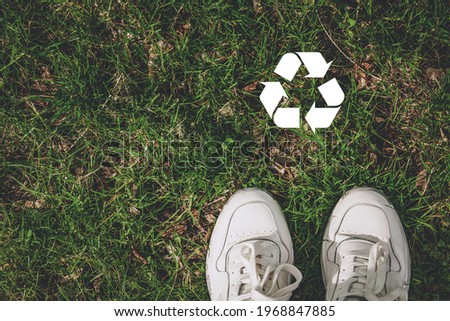 Recycling logo symbol in white.Concept of recycling the plastic, ecology, environmental conservation. Closeup top view of legs, white sneakers.Shoes walking on grass.Copyspace for text, flatly, banner Royalty-Free Stock Photo #1968847885