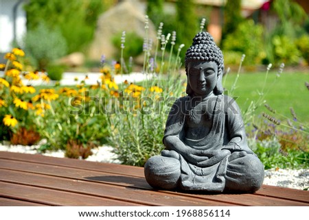 A closeup of a small Buddha statue in a garden with a blurry background Royalty-Free Stock Photo #1968856114