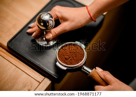 Close-up of barista hand tamping coffee in portafilter before making fresh drink in coffee machine at coffee shop. Royalty-Free Stock Photo #1968871177