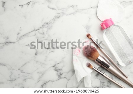 Dirty tissue, cotton pads, brushes and micellar cleansing water on white marble background, flat lay. Space for text